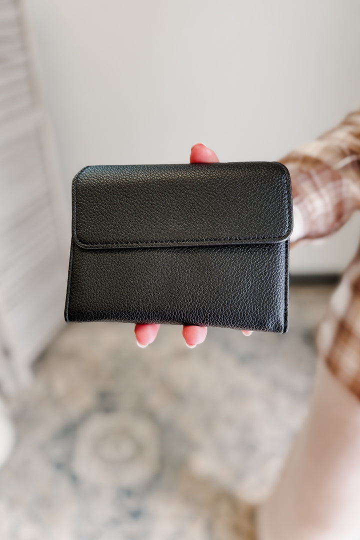 Person holding a black leather wallet against a neutral background