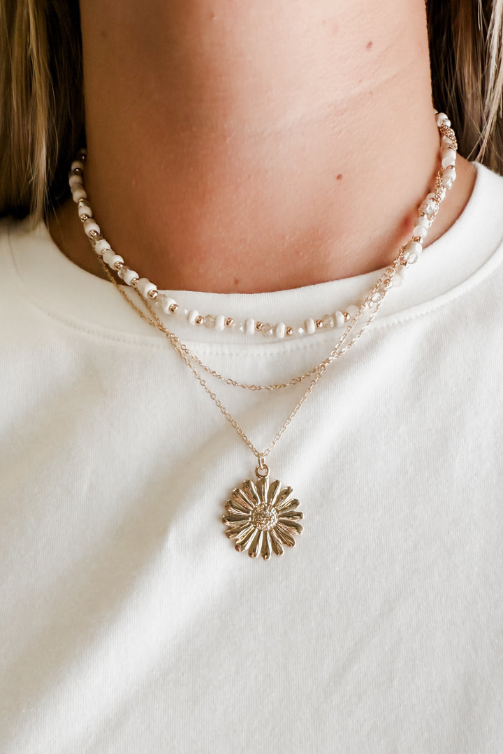 Close-up of a person wearing a pearl necklace and a gold sun-shaped pendant on a white background