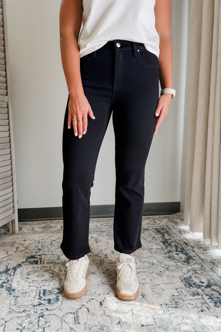 Person wearing black pants and white sneakers in a room with a patterned rug and neutral walls.