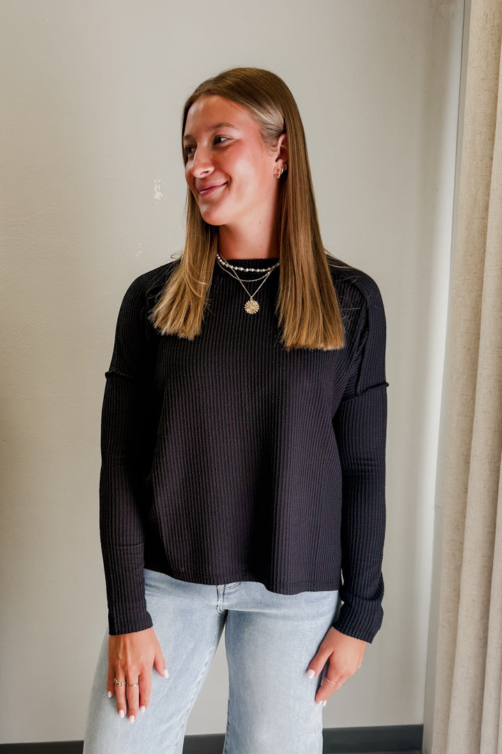 Woman wearing a black ribbed sweater and light blue jeans against a neutral background