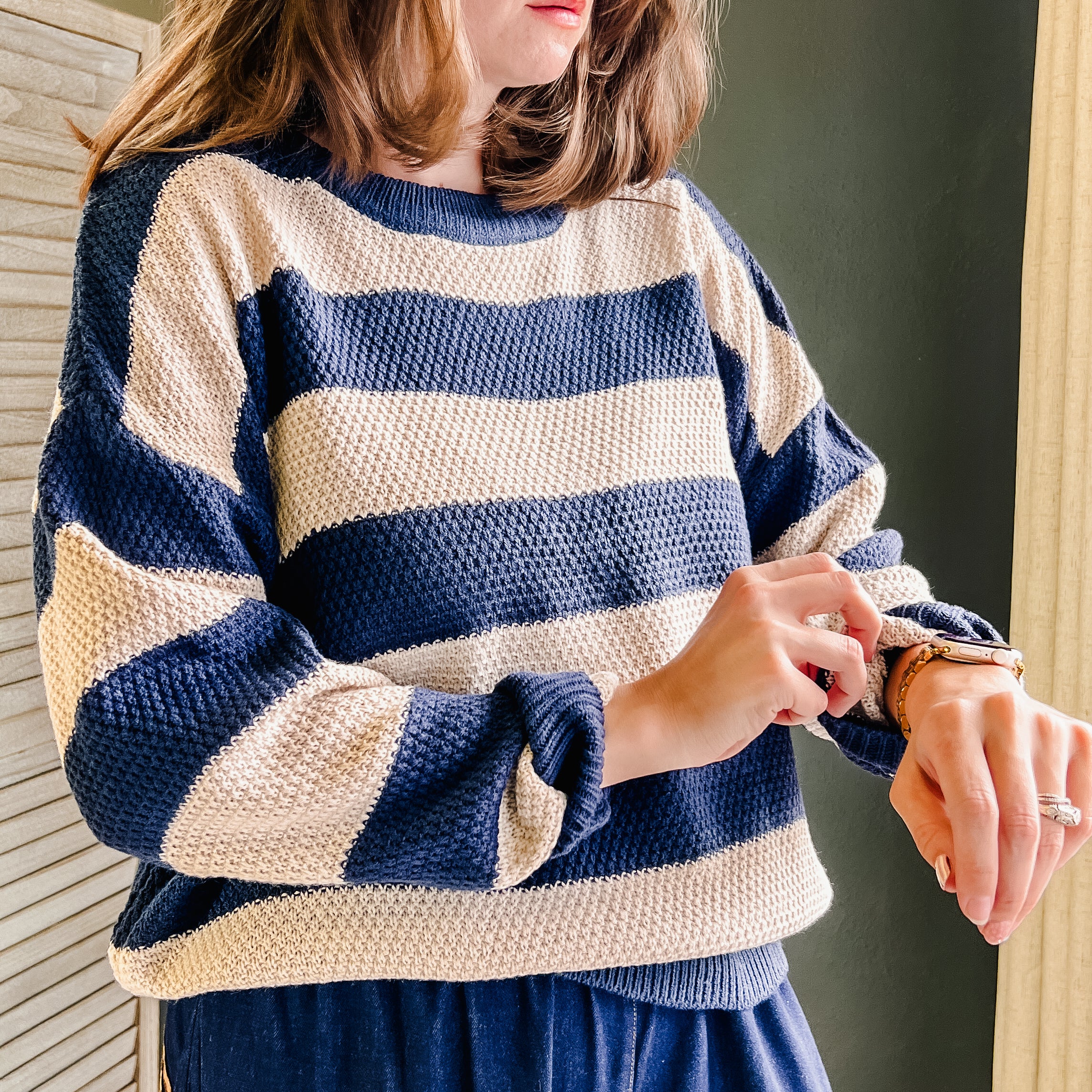 A woman wearing a navy and cream waffle-knit long-sleeve sweater and navy pants, looking down while adjusting her watch.