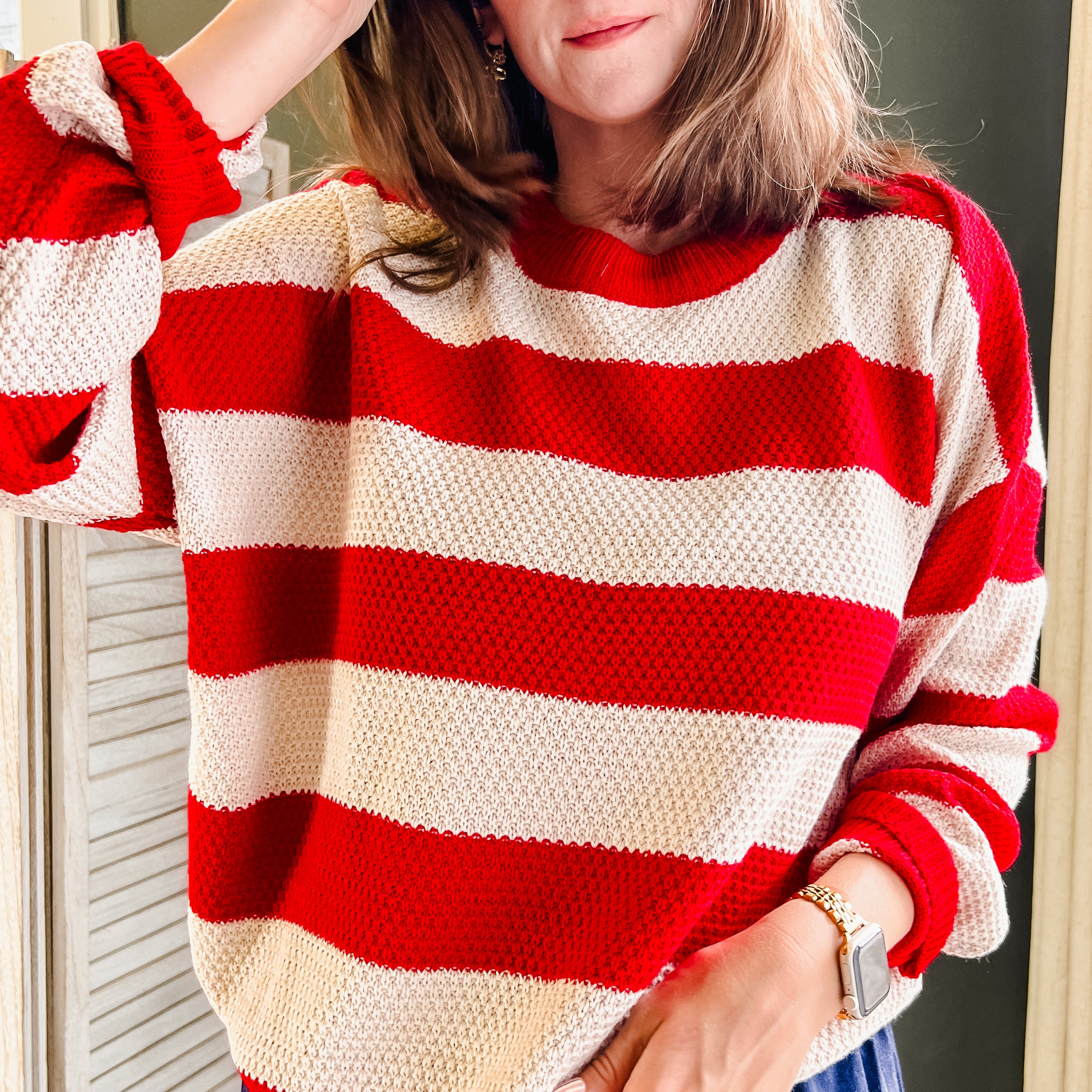 A woman wearing a red and cream striped knit sweater with blue pants, standing indoors.