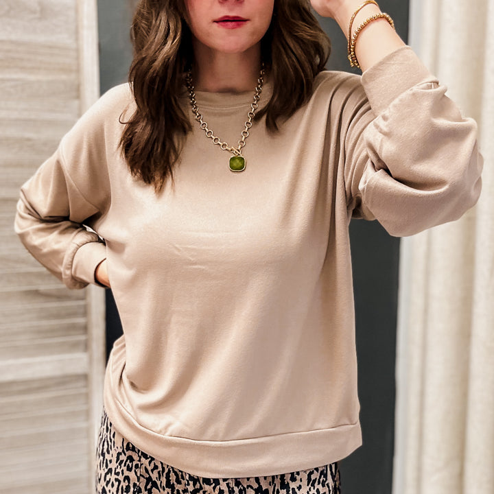 A woman wearing a beige long-sleeve crewneck sweatshirt and leopard print pants, posing in front of a mirror.