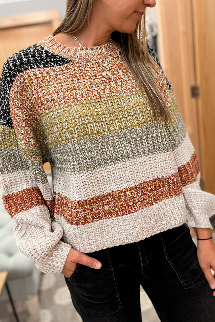 Person wearing a multicolored striped sweater with a blurred indoor background
