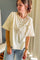 A woman wearing a cream-colored short-sleeve henley top with a button placket and chest pocket, paired with light blue jeans, standing in an indoor setting.
