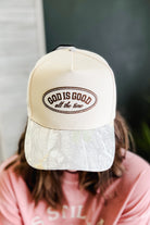 A person wearing a cream-colored trucker cap with a brown embroidered oval logo that reads 'GOD IS GOOD all the time'. The cap features a white patterned brim and is shown from the back, obscuring the person's face.