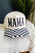 A cream-colored baseball cap with 'MAMA' embroidered in black across the front and a black-and-white checkered pattern on the visor, resting on a textured cream throw blanket.