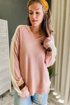 A woman wearing a dusty pink waffle-knit long-sleeve sweater with cream-colored contrast panels on the sleeves and cuffs, paired with light blue jeans and a mustard yellow headband.