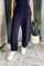 A person wearing dark navy wide-leg sweatpants with an elastic waistband, paired with white sneakers, standing in an indoor setting with a patterned rug and a potted plant.