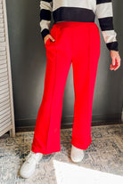 A person wearing bright red wide-leg pants, a black and white striped long-sleeve top, and white sneakers, standing indoors against a dark gray wall.