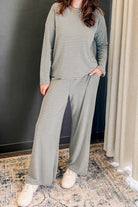 A woman wearing a matching two-piece loungewear set with a muted green and white horizontal stripe pattern, featuring a long-sleeve top and wide-leg pants, paired with white sneakers.