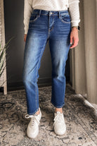 A person wearing medium-wash blue denim jeans with a faded wash, styled with a white knit sweater and white sneakers in an indoor setting.