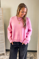 Woman wearing a pink sweater and dark jeans indoors.