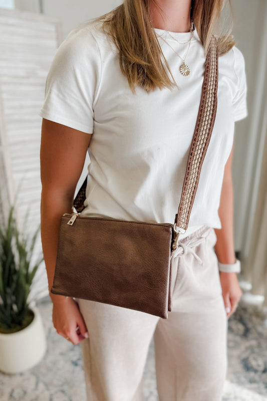 Person wearing a white shirt and beige pants with a brown crossbody bag indoors.
