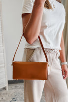 Person wearing a white top and beige pants with a brown leather handbag.