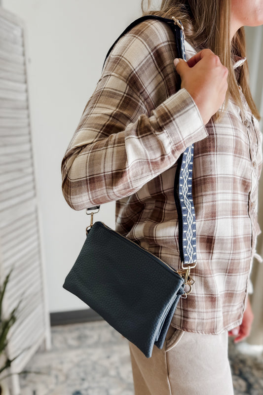 Person wearing a plaid shirt holding a navy handbag indoors.