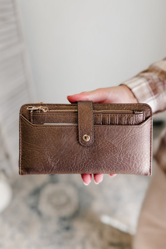 Brown leather wallet held by a person against a blurred background