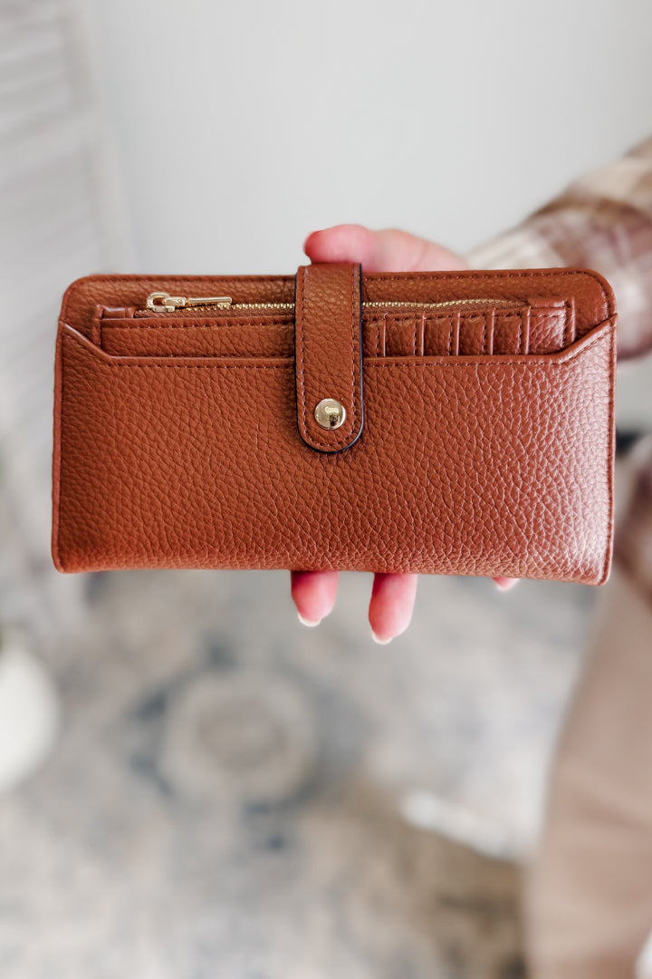 Brown leather wallet held by a hand against a blurred background
