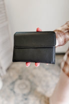 Person holding a black leather wallet against a neutral background