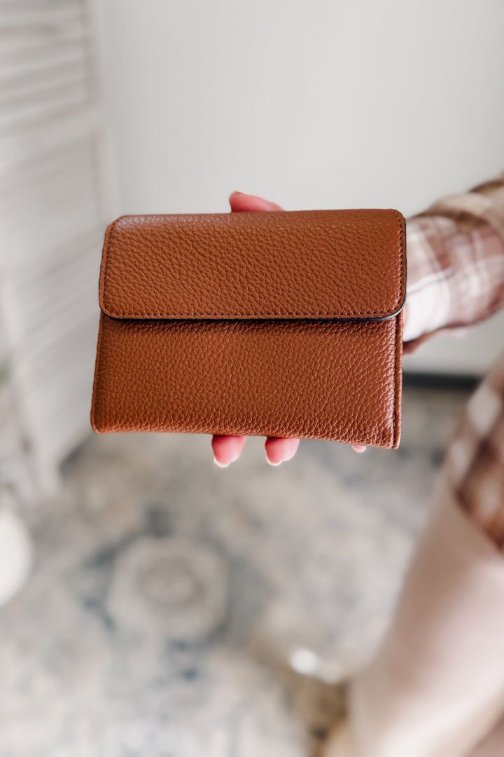 Brown leather wallet held by a person with a blurred background