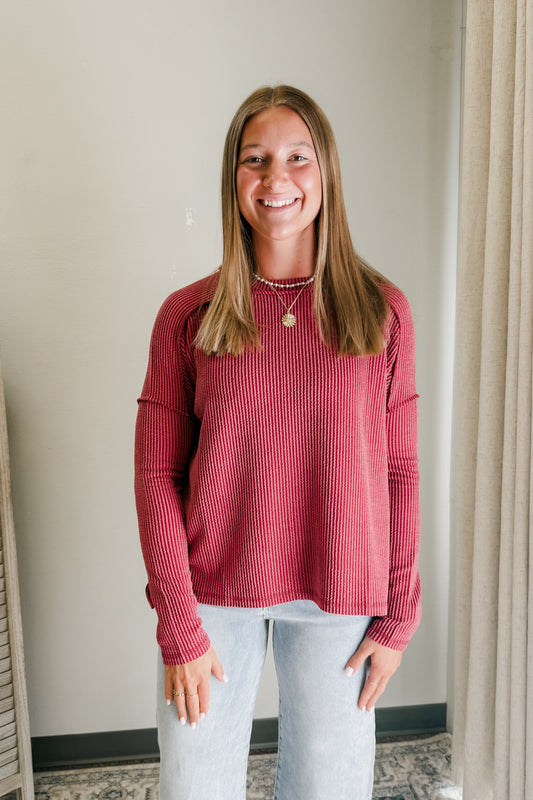 Woman wearing a red ribbed sweater and light blue jeans indoors.
