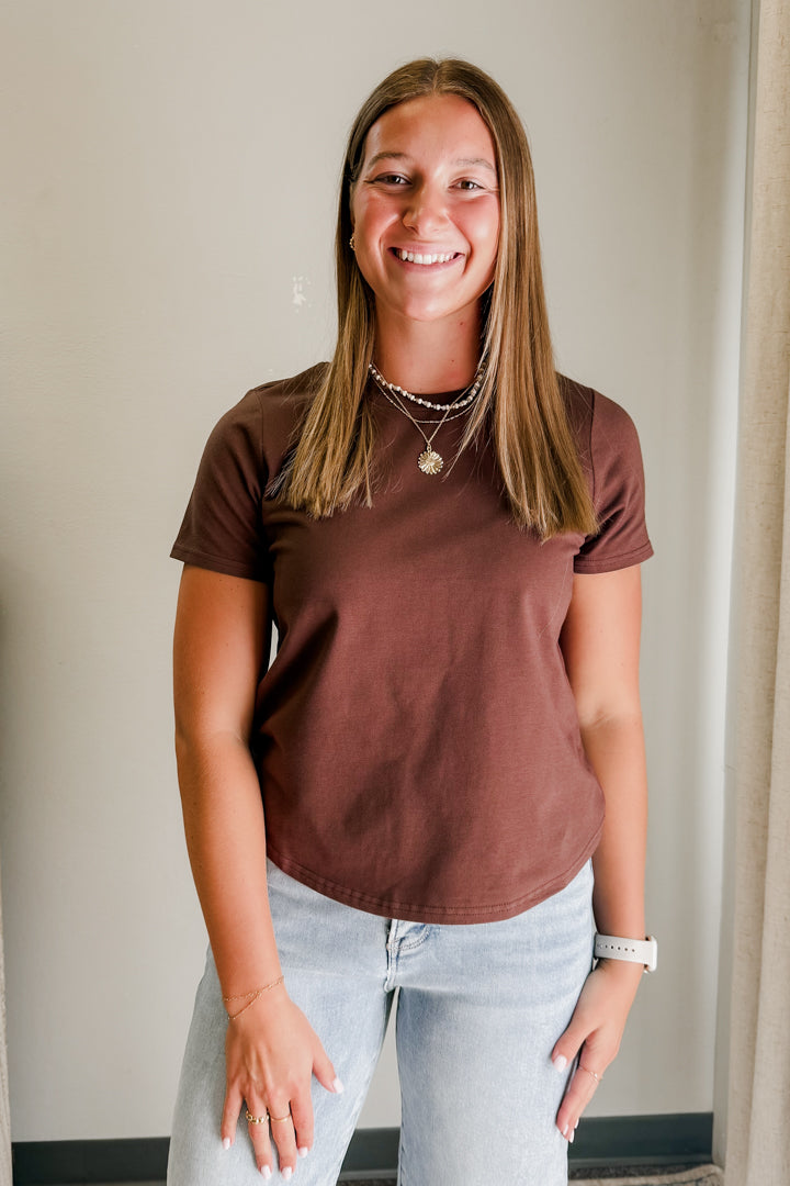 Person wearing a brown t-shirt and light blue jeans against a plain background