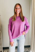 Woman wearing a pink ribbed sweater and light blue jeans indoors.