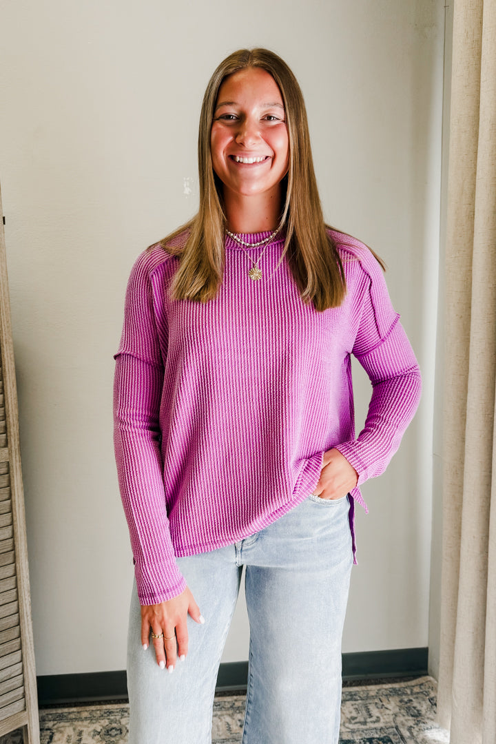 Woman wearing a pink ribbed sweater and light blue jeans indoors.