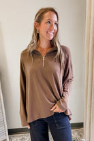 Woman wearing a brown long-sleeve top with a zipper, standing indoors.