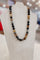 A beaded necklace made of polished round gemstone beads in black, brown, gray, and translucent amber tones, displayed on a white jewelry bust.