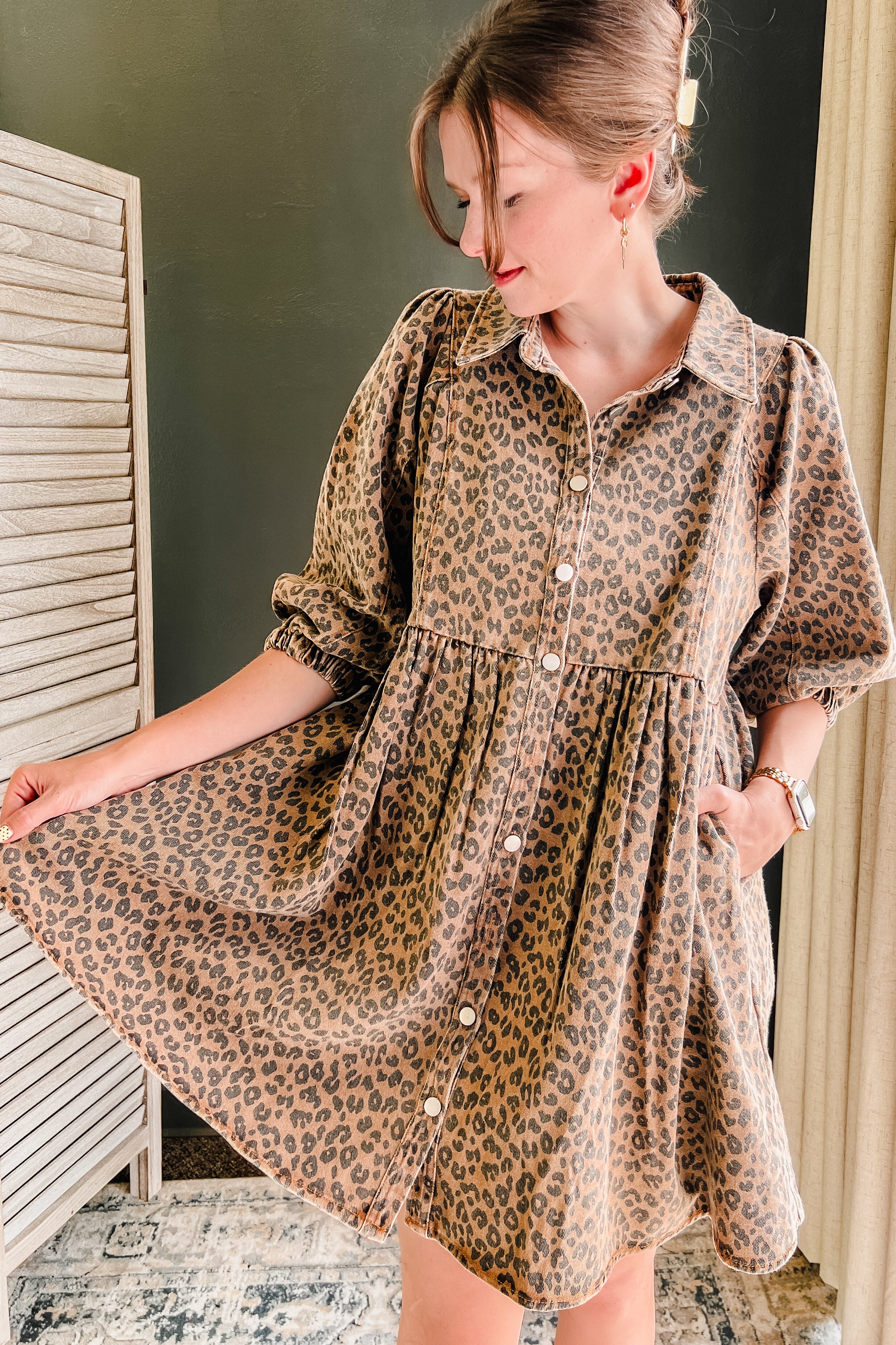 A woman wearing a brown and black leopard print shirt dress with puff sleeves and a button-down front, standing in an indoor setting.