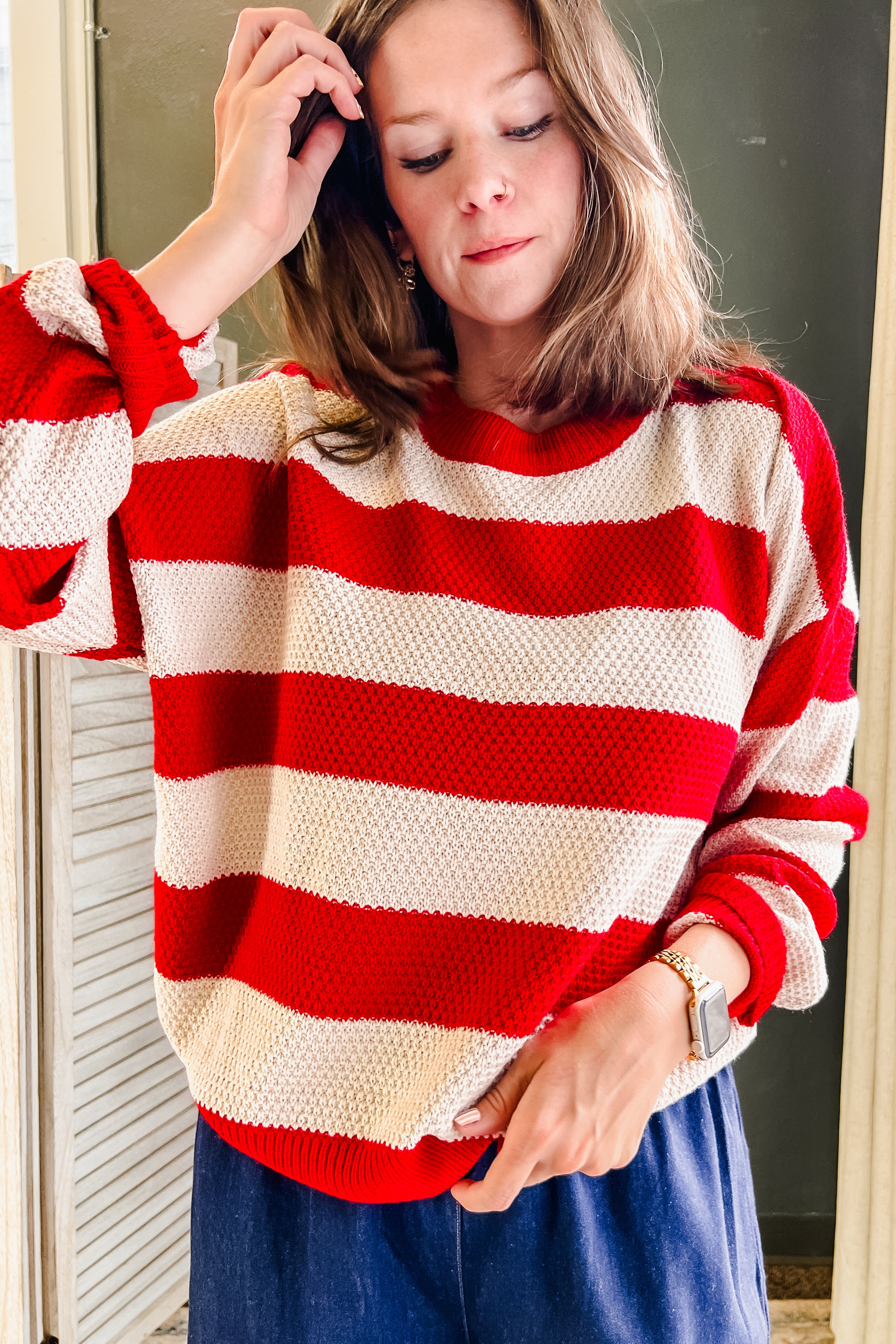 A woman wearing a red and cream striped knit sweater with blue pants, standing indoors.