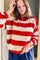 A woman wearing a red and cream striped knit sweater with blue pants, standing indoors.
