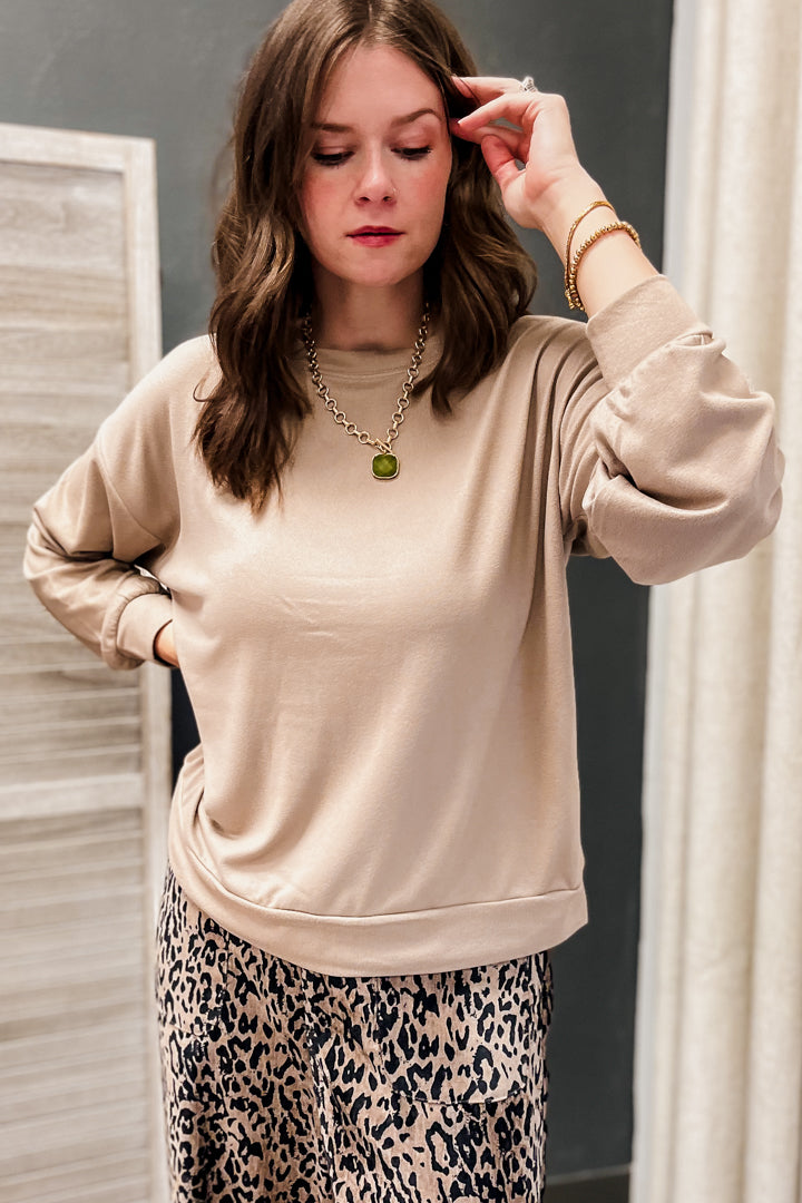A woman wearing a beige long-sleeve crewneck sweatshirt and leopard print pants, posing in front of a mirror.