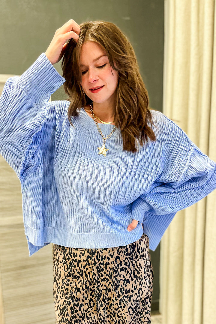 A woman wearing a light blue waffle-knit long-sleeve sweater and a leopard-print skirt, standing indoors with a neutral background.