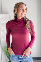 Woman wearing a maroon long-sleeve top and blue jeans indoors.