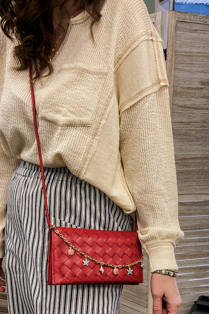 A woven slim envelope with a playful metal sea-inspired charm chain red