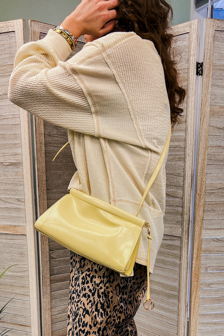A small bag with an adjustable strap, top-frame closure and ring-tassel hardware yellow