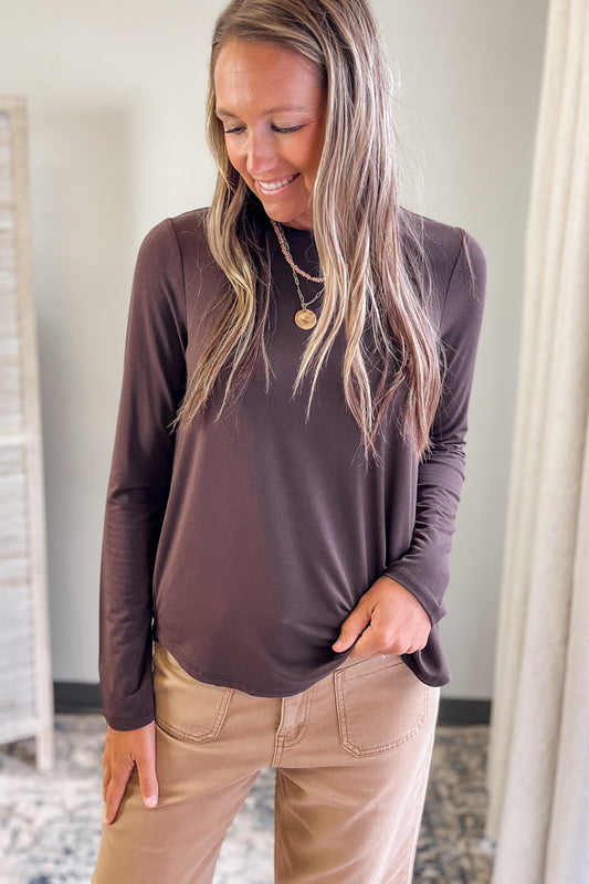 Woman wearing a brown long-sleeve top and beige pants indoors.