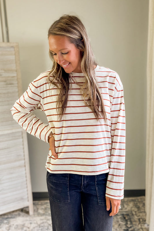 Woman wearing a striped long-sleeve shirt and dark jeans indoors.